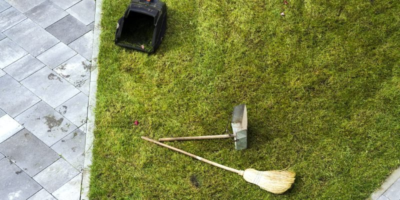 Jug dustpan and a broom on a green grass lawn. Gardening tools.